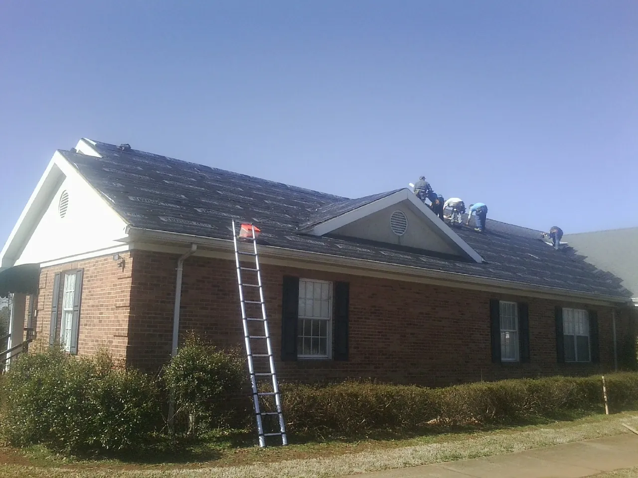 Crew tearing shingles off a brick ranch roof with a ladder set — Emergency Roof Repair work by our crew in Perry Hall
