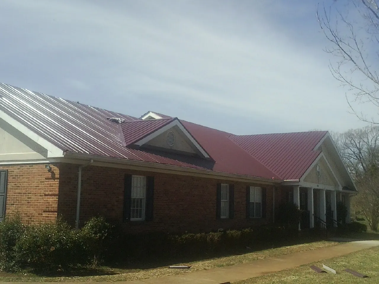 Red metal roof with gabled entries on a long brick building, from a Hail Damage Roof Repair job in Perry Hall