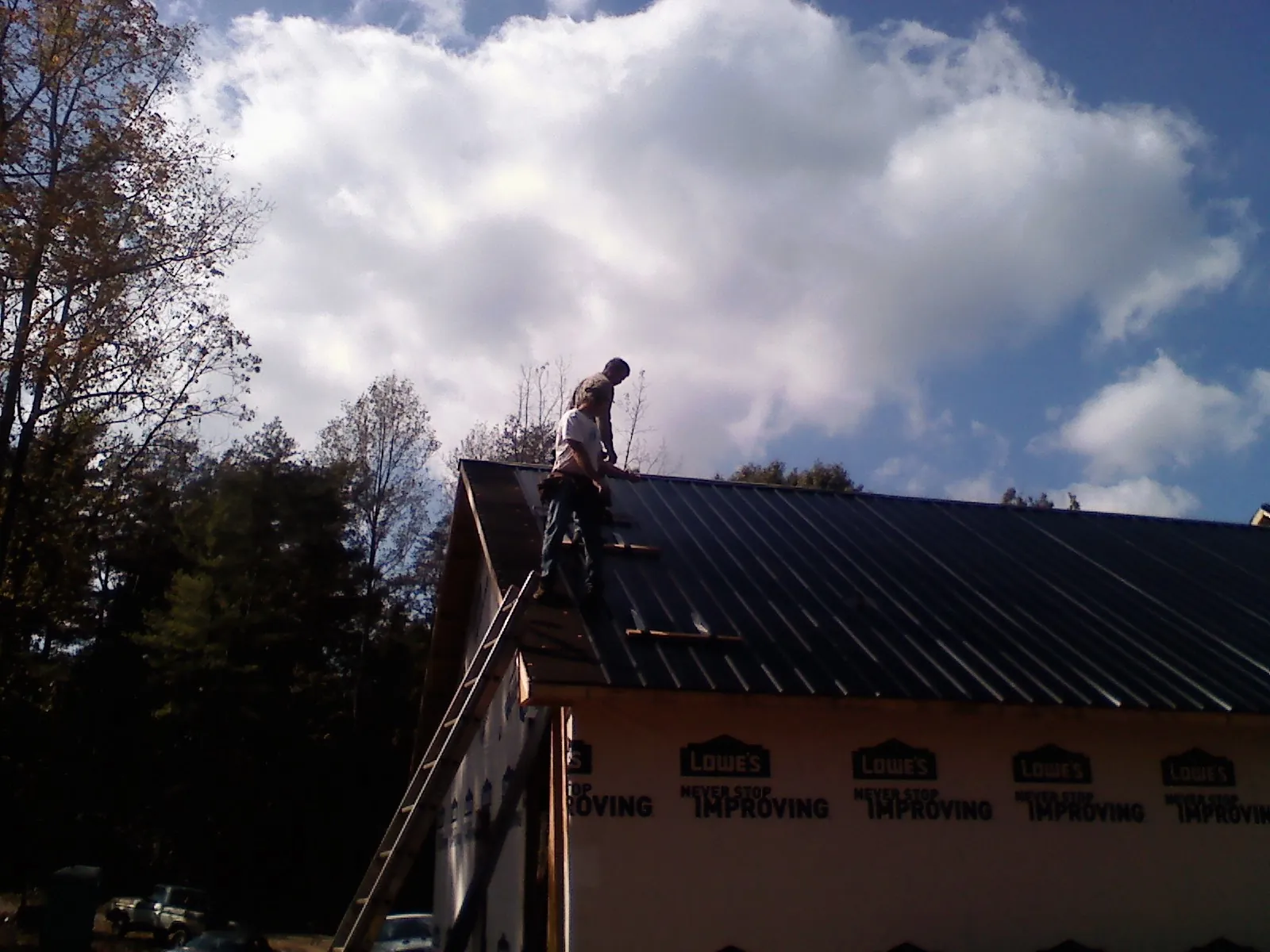 Roofer fastening dark metal panels high against a cloudy sky, from a Roof Inspection job in Perry Hall
