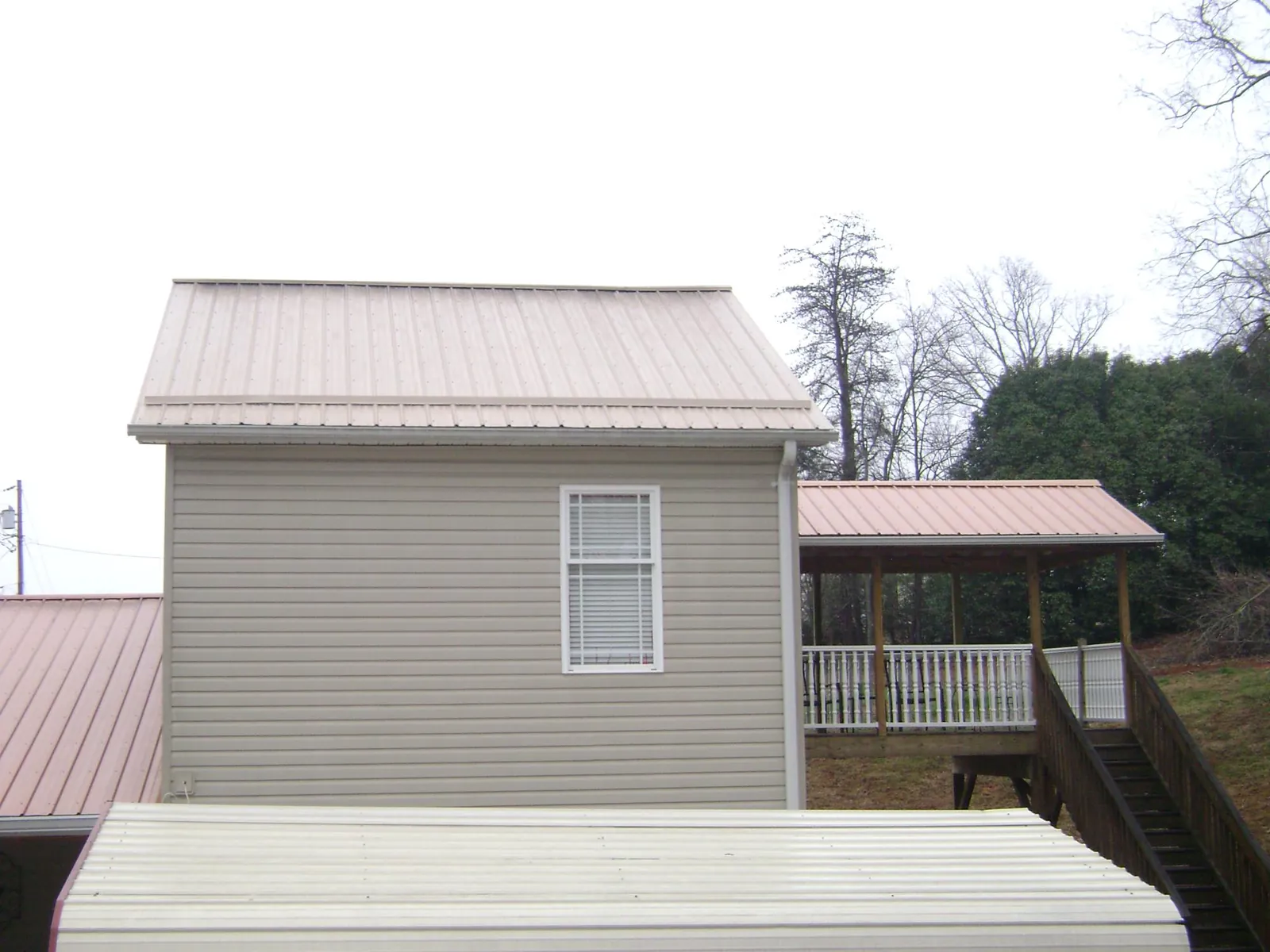 Tan metal roofs on a two story addition and attached porch, from a Roof Replacement job in Perry Hall